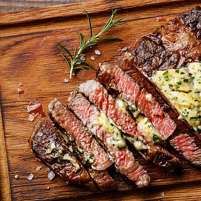 Sliced grilled Medium rare barbecue steak Ribeye with herb butter on cutting board close up